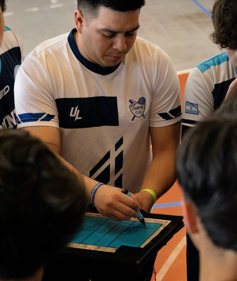 Técnico deportivo anotando una jugada en una pizarra táctica junto a su equipo